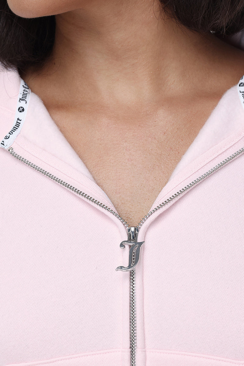 A close-up of a person wearing the Embroidered Knit Cropped Hoodie in light pink, partially unzipped to reveal a silver “J” charm on the zipper pull. This hoodie features white fabric lining with black text at the collar and an embroidered logo for a signature touch.