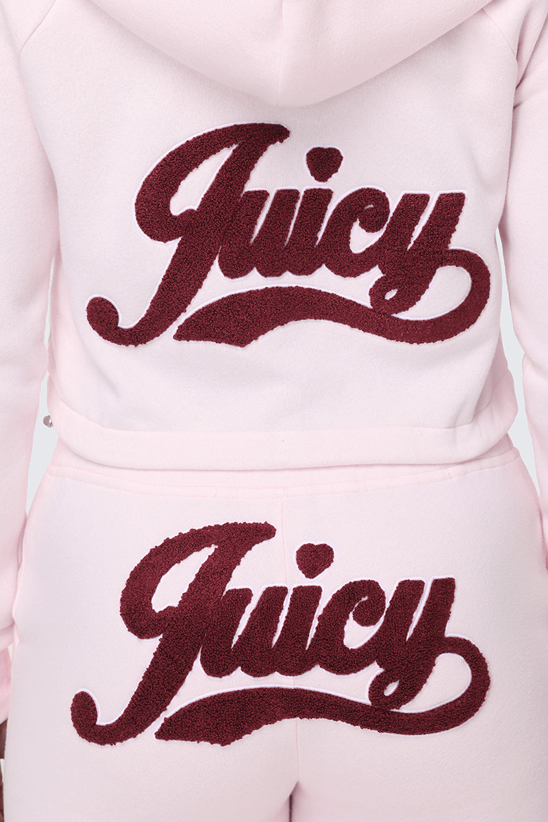 A person is seen from the back wearing a light pink Embroidered Knit Cropped Hoodie velour tracksuit, featuring dark red textured "Juicy" embroidery in large letters on both the hoodie and matching pants.