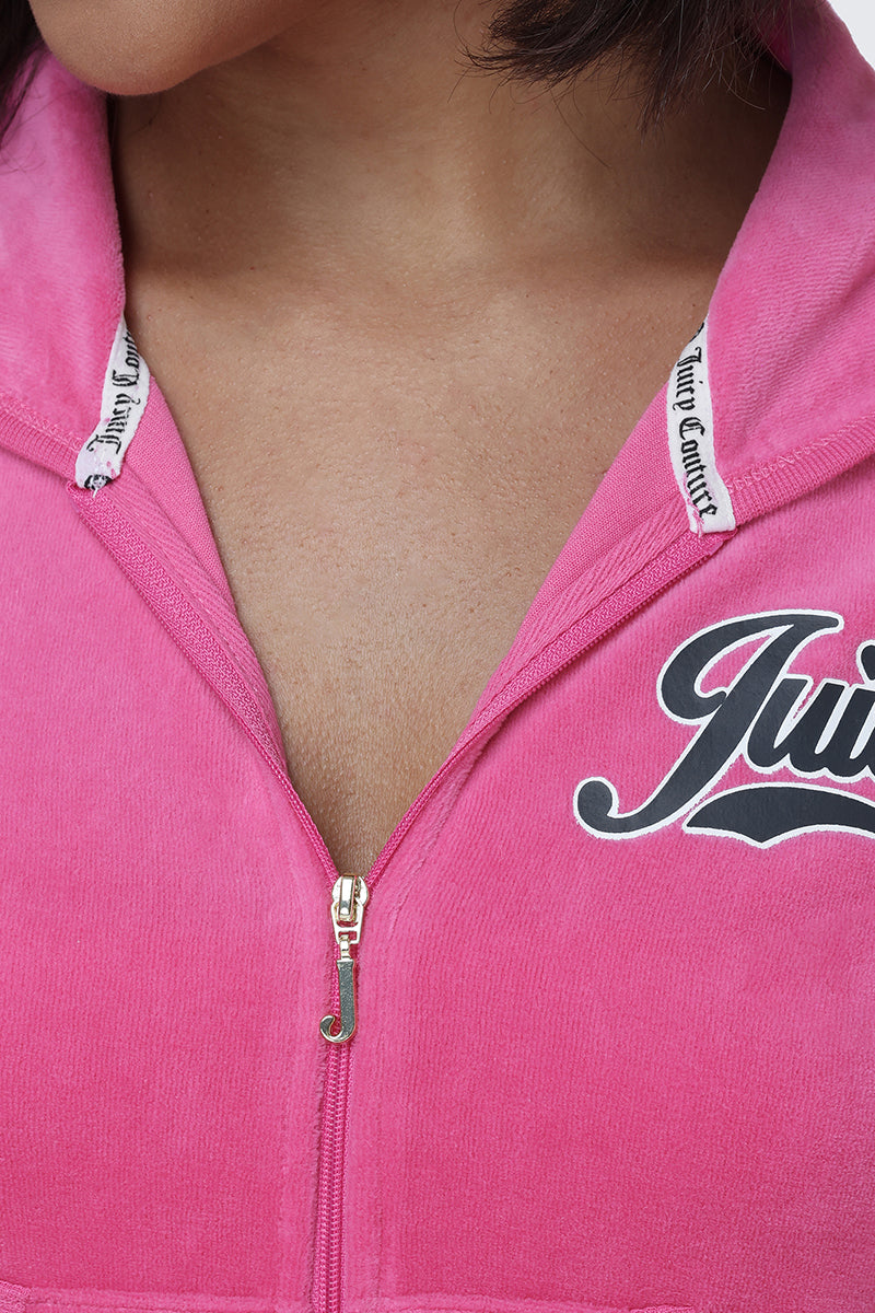 A close-up of a person wearing the Cotton Velour Hoodie in pink, partially unzipped to reveal branded trim and the signature script logo along the collar.