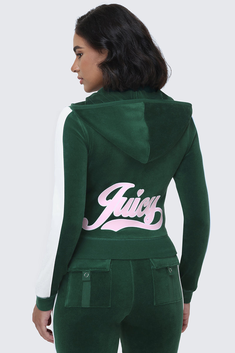 A woman is seen from behind wearing the Cotton Velour Hoodie in green, featuring white accents on the sleeves and a bold pink "Juicy" signature script logo across the back of the sporty hooded jacket.