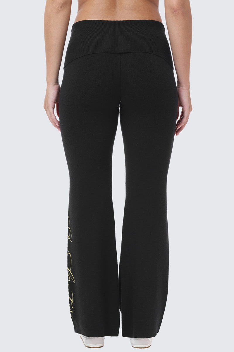 Back view of black Embroidered Knit Flare Pants featuring a wide, fold-over waistband and gold embroidery along the side of the leg.