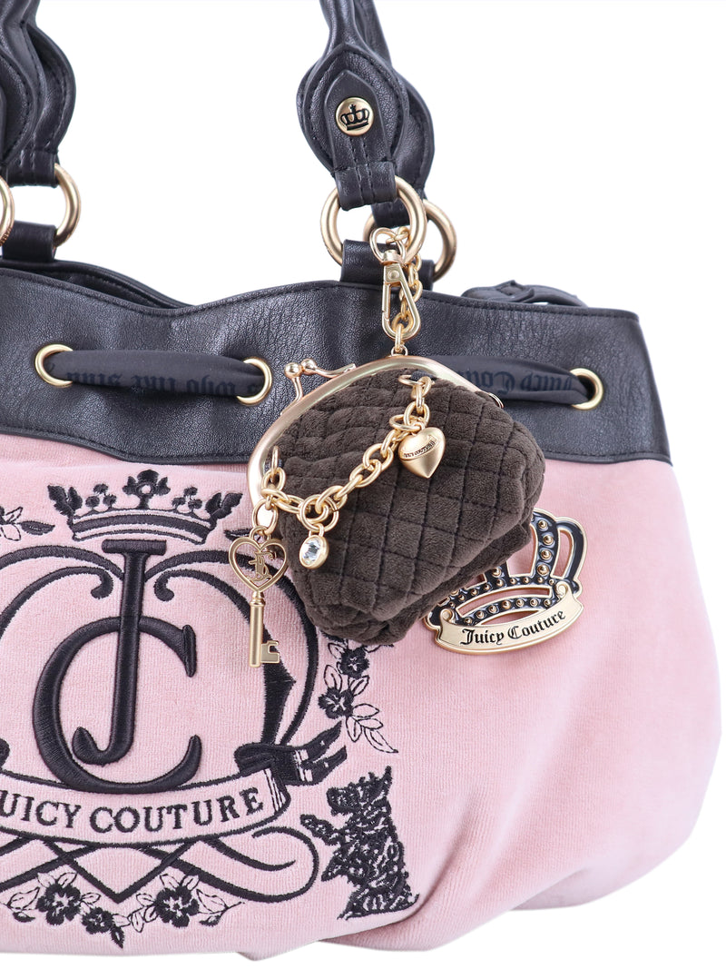 A pink Crowns & Kisses Satchel Bag with black leather trim and a large logo, featuring a small quilted coin purse, a gold key charm, and a jeweled crown charm hanging from the handle.