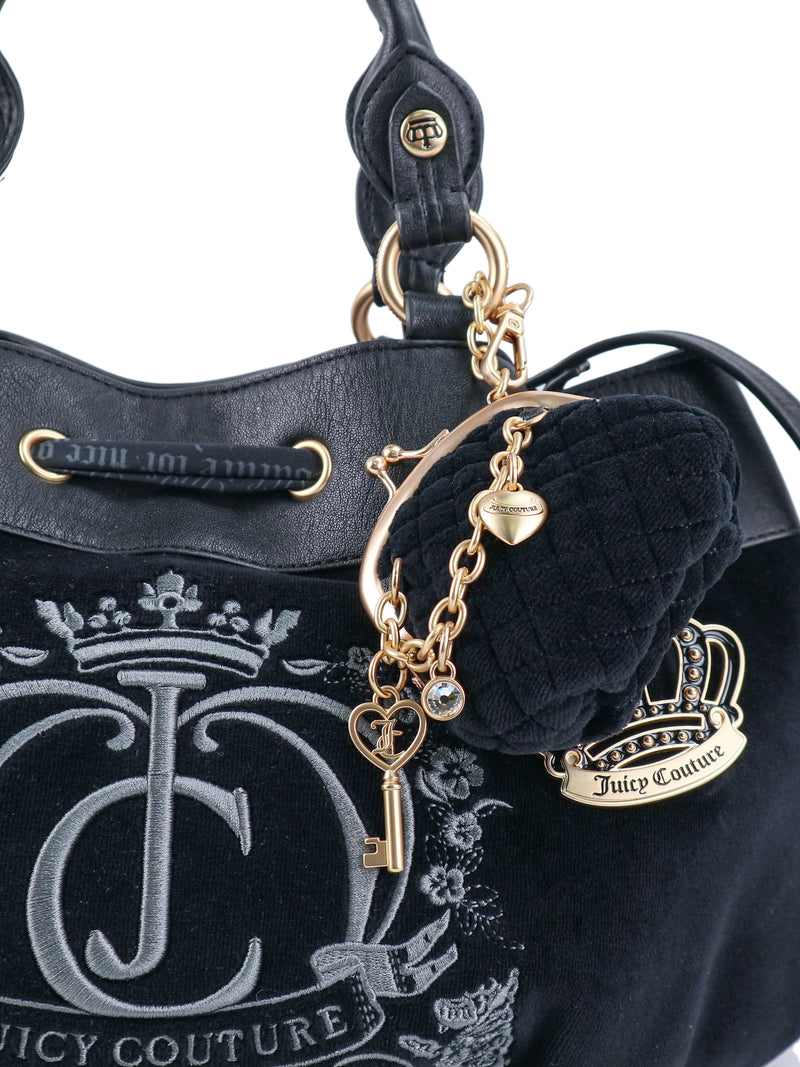 Black velvet Y2K Crowns & Kisses Satchel Bag featuring an embroidered logo, a drawstring closure, and gold-tone metal charms including a heart, a key, and a small coin purse.