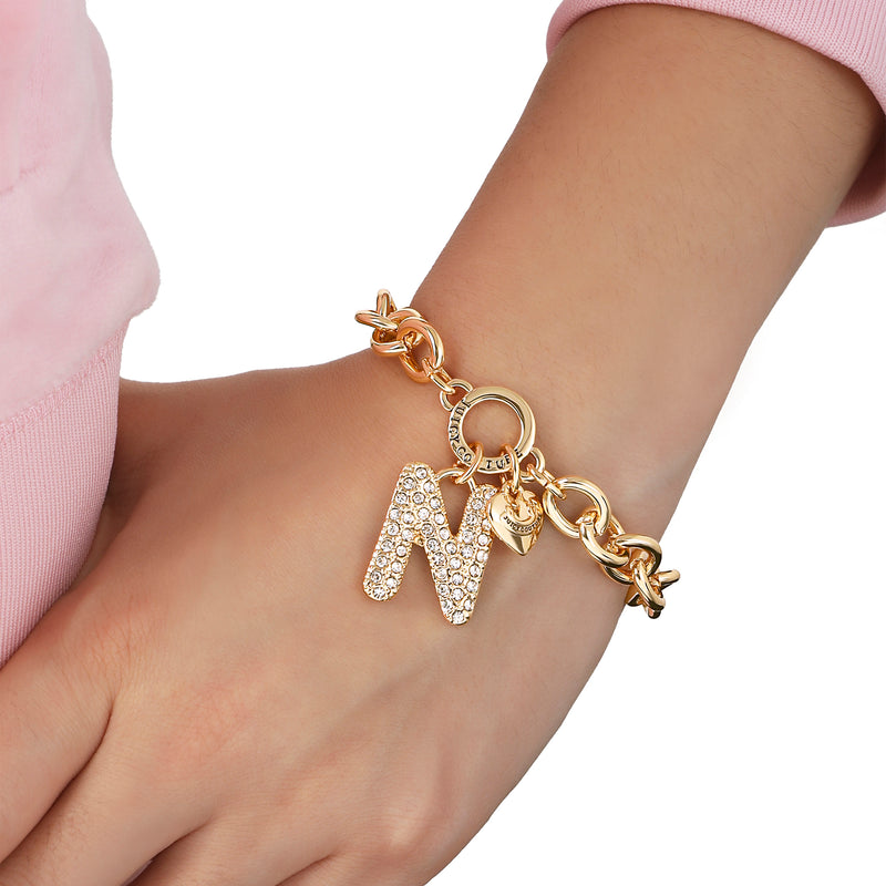 Worn on the wrist with a light pink long-sleeve top, the Pavé Initial Charm Bracelet, Letter N features a gold chunky design adorned with a large rhinestone-studded “N” charm and a small heart charm for an elegant finishing touch.