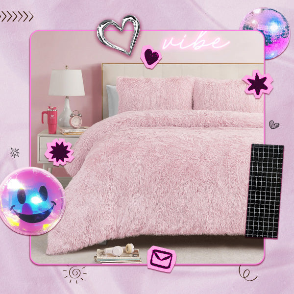 A pink fluffy faux-fur bedding set, including a duvet cover and two matching pillowcases, styled on a bed in a bedroom scene. The image has a retro 90s aesthetic with pink borders, a disco ball, a smiley face bubble, and decorative stickers.