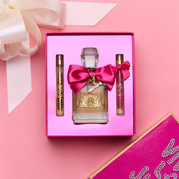 Perfume set with a bottle and two travel-sized bottles in a pink box on a pink background.