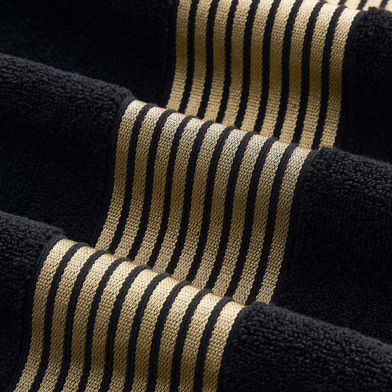 A close-up of textured fabric with black and gold stripes, showcasing raised and flat sections for a wavy 3D effect like the premium weave found in the Melissa Bath Towel Set.
