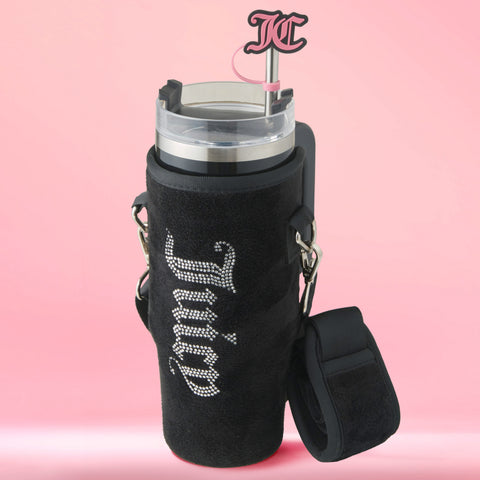The Jetsetter Hydration Stainless Steel Tumbler with a neoprene crossbody pouch features a black exterior, rhinestone Juicy Couture logo, pink straw with JC initials, and is shown against a pink background.