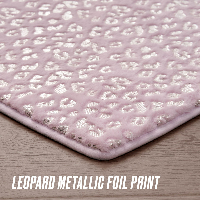 A close-up of the Metallic Leopard Plush Rug, 3' Heart, in soft light pink with a shiny metallic leopard print pattern, shown on a wooden floor. Text at the bottom reads Leopard Metallic Foil Print.