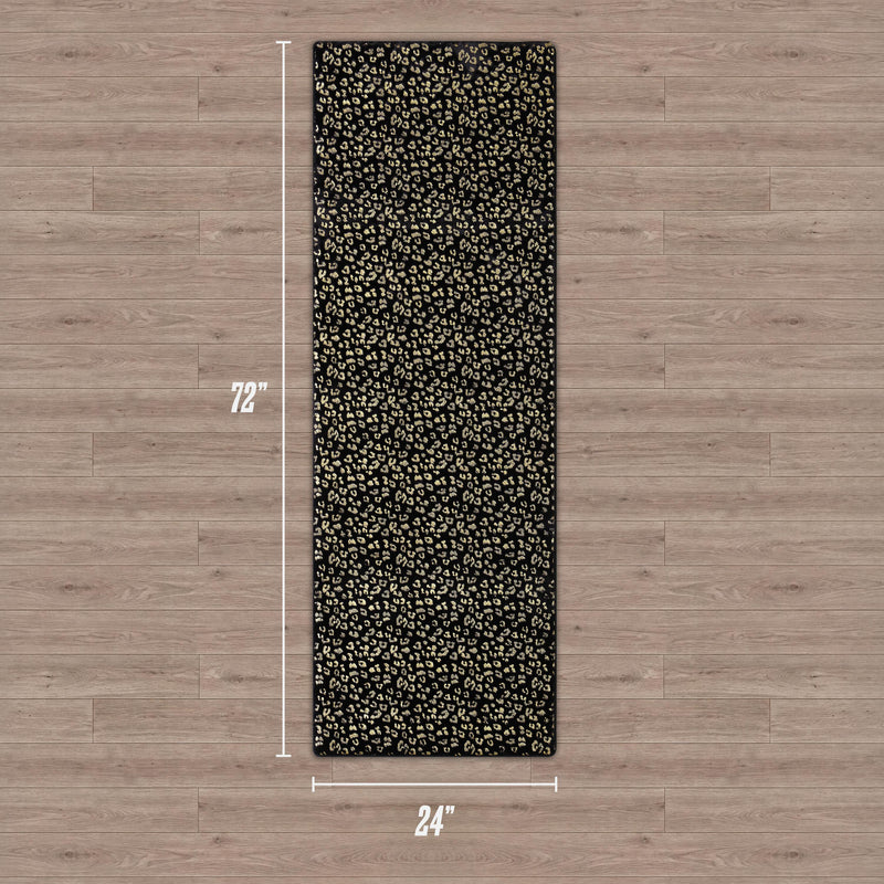 The Metallic Leopard Plush Rug, 2' x 6', features a black surface with a gold leopard print and lies on a wooden floor. White measurement lines and text display its dimensions.