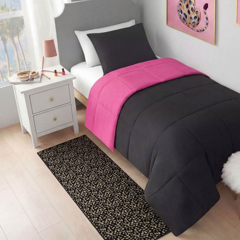 A neatly made twin bed with black and hot pink bedding is next to a white nightstand with makeup items and a lamp. A Metallic Leopard Plush Rug, 2' x 6', lies on the light wood floor. Art with a pink and leopard design hangs above.