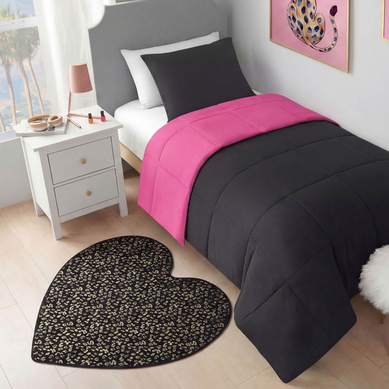 A neatly made bed with a black comforter and bright pink blanket sits by a white nightstand. On the floor is a Metallic Leopard Plush Rug, 3' Heart, and colorful leopard wall art hangs above the bed.