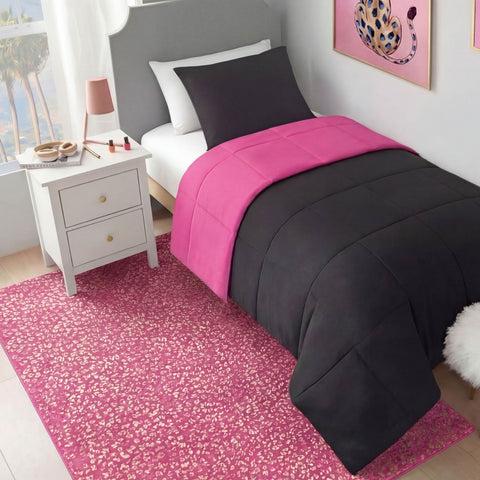 A neatly made bed with a black and hot pink comforter, black pillow, and white headboard sits beside a white nightstand with a lamp and makeup. A Metallic Leopard Plush Rug (4' x 6') covers the floor and pink leopard art hangs on the wall.