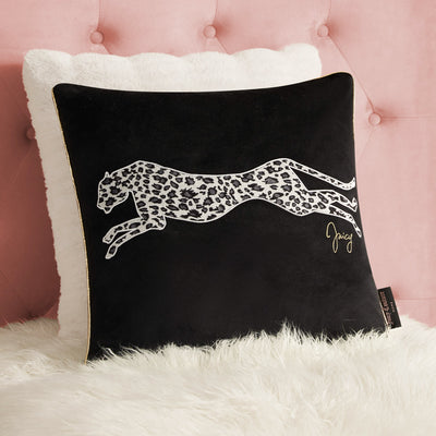 A Velvet Cheetah Square Pillow with "Juicy" in gold rests on a white furry pillow against a pink tufted background, adding glamorous style as the perfect decorative accent.