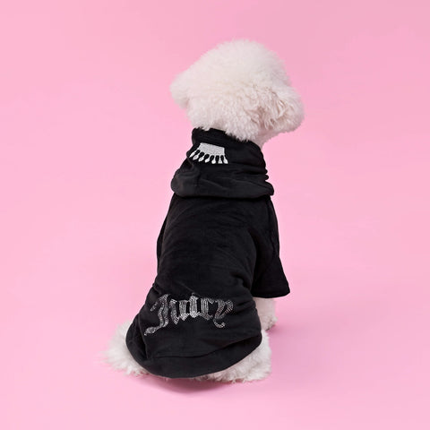A fluffy white dog sits facing away, wearing the Bling Velour Pet Hoodie adorned with sparkling rhinestone details and the word “Juicy” on the back—an iconic piece of designer pet apparel—against a solid pink background.