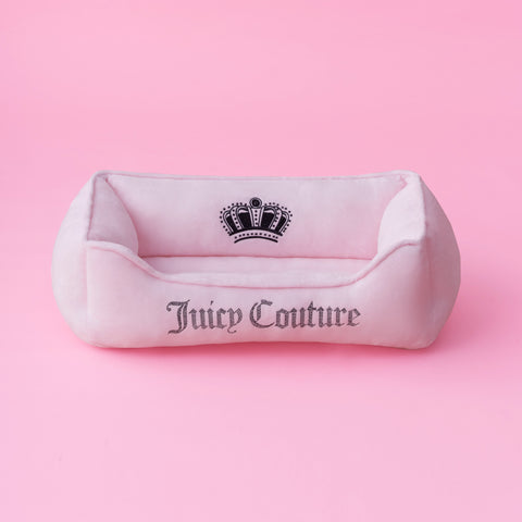 A black velour pet bed with Juicy Couture and a crown logo embroidered on the front, featuring subtle bling accents and set against a black background.