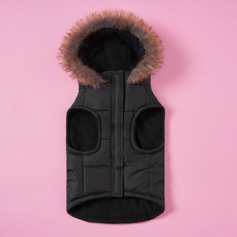 A Pet Faux Fur Hooded Jacket by Juicy Couture is displayed on a pink background. This black quilted jacket features a faux fur-trimmed hood, convenient leg openings, and a central zipper—making it the perfect cold-weather gear for dogs.