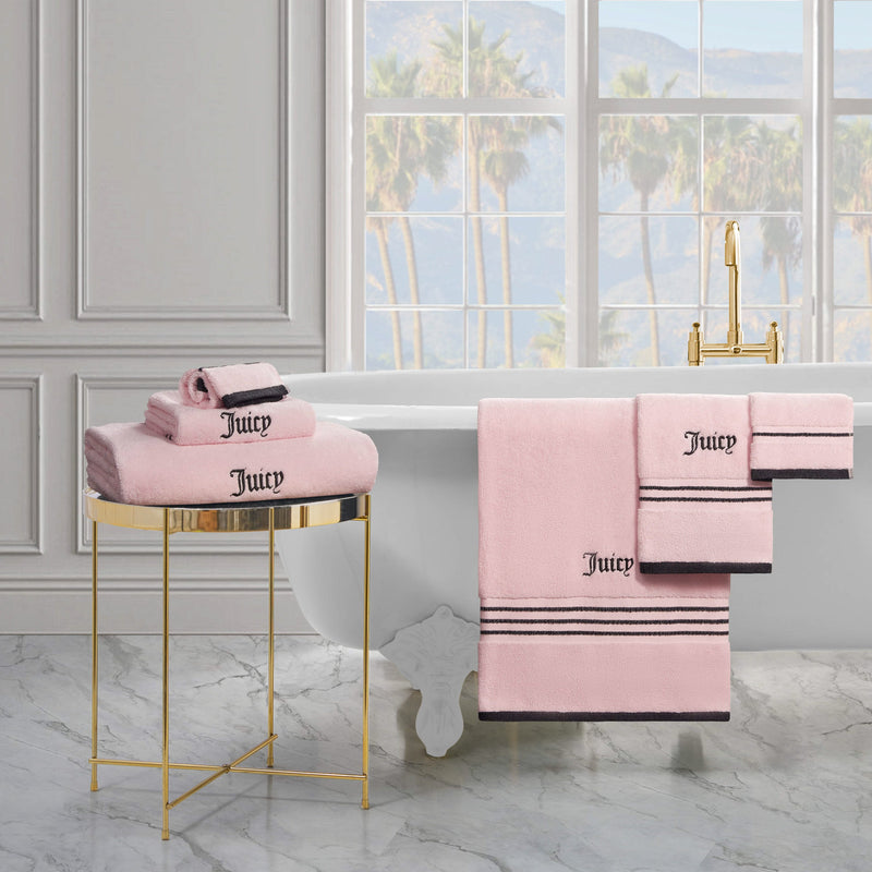 A luxurious white bathtub and gold faucet in a bright bathroom with marble floors, a gold side table, and neatly folded Neon Border Bath Towel Set. Palm trees and mountains are visible through the window.