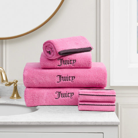 A Neon Border Bath Towel Set is neatly stacked on a white bathroom countertop near the sink and mirror. One plush bath towel is rolled, while two washcloths are folded next to the stack.