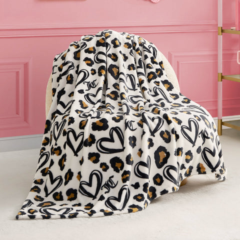 The Plush Throw Blanket, ultra-soft with a white base and black heart leopard print, is draped over a cream chair in a pink-walled room.