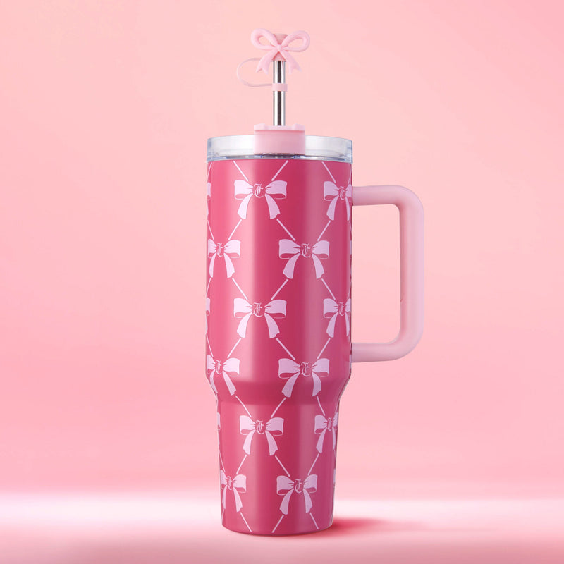 The Jetsetter Hydration Stainless Steel Tumbler, 40 oz, in tall pink with a handle and white bow accents, sits on a soft pink background. It features a clear lid and straw topped with a pink bow-shaped decoration for stylish sipping.