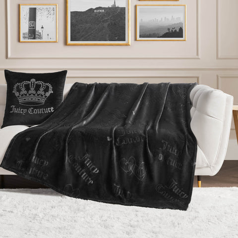 A white couch with a black Juicy Couture pillow and an Embossed Plush Throw Blanket sits in a stylish living room with framed wall art and a white rug on the floor.
