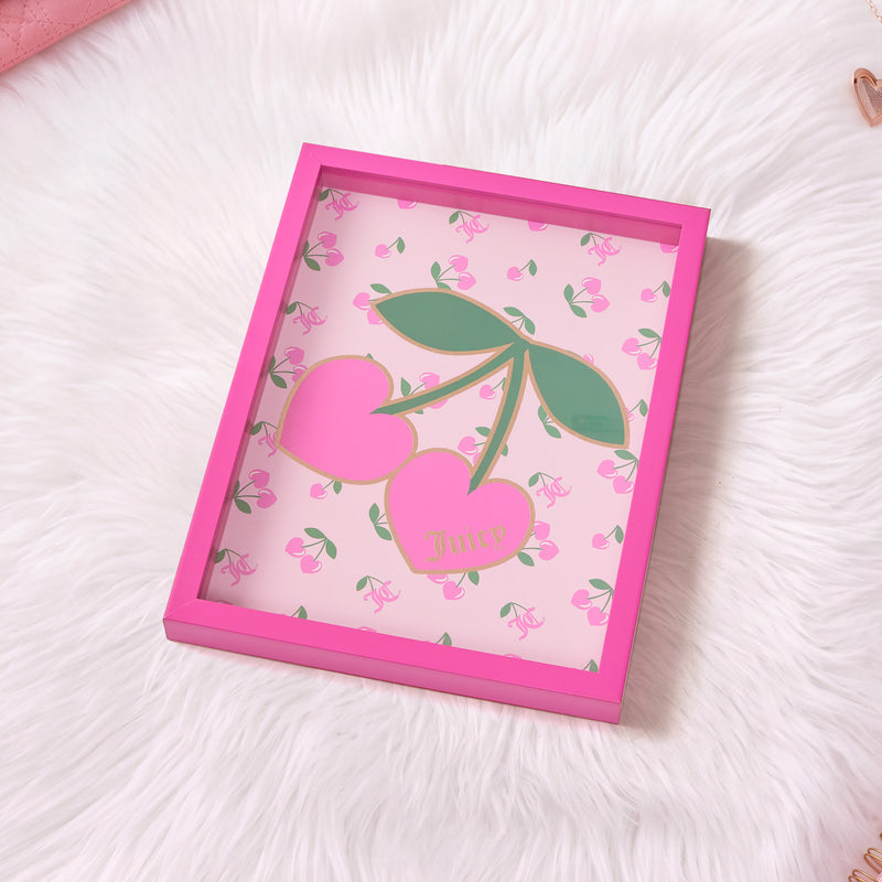 A pink-framed Shadow Box Wall Art (12″ x 16″) features two oversized cherries with green leaves, set against a backdrop adorned with small cherry patterns and playful Juicy text. Displayed on a white fur surface, this fashion-inspired piece channels iconic Juicy Couture style, making it a chic decorative addition to any room.