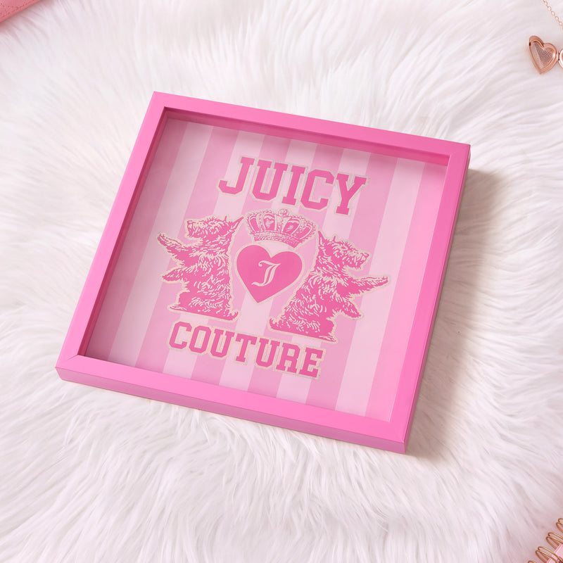 The Shadow Box Wall Art, 14″ x 14″, features a pink frame, two lion illustrations, and a crowned heart logo set against a striped pink background; displayed on a white fluffy surface, it creates stunning fashion-inspired decor for any space.
