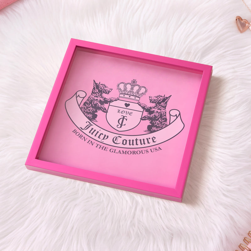 A 14″ x 14″ Shadow Box Wall Art sits on white faux fur, featuring Juicy Couture’s pink design with two dogs, a crown, and the phrase “Born in the Glamorous USA”—making it a standout piece that perfectly captures fashion-inspired artwork.