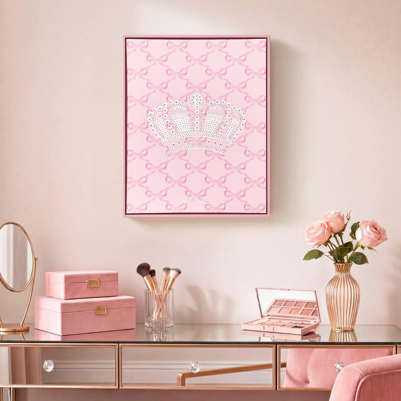 A vanity table with a mirror, makeup brushes, pink boxes, and a vase of pink roses. Above the table hangs the Shadow Box Wall Art, 16″ x 20″, featuring a jeweled crown on a pink patterned background in a Juicy Couture style, bringing fashion-inspired glamour to the space.