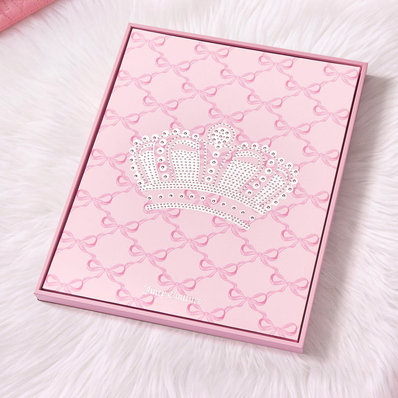 A pink Shadow Box Wall Art (16″ x 20″) with a jeweled crown design and bow pattern rests on white fur, capturing a fashion-inspired artwork aesthetic. Featuring “Juicy Couture” written at the bottom in small letters, this piece makes an elegant addition to any chic space as stylish Juicy Couture wall art or sophisticated shadow box décor.