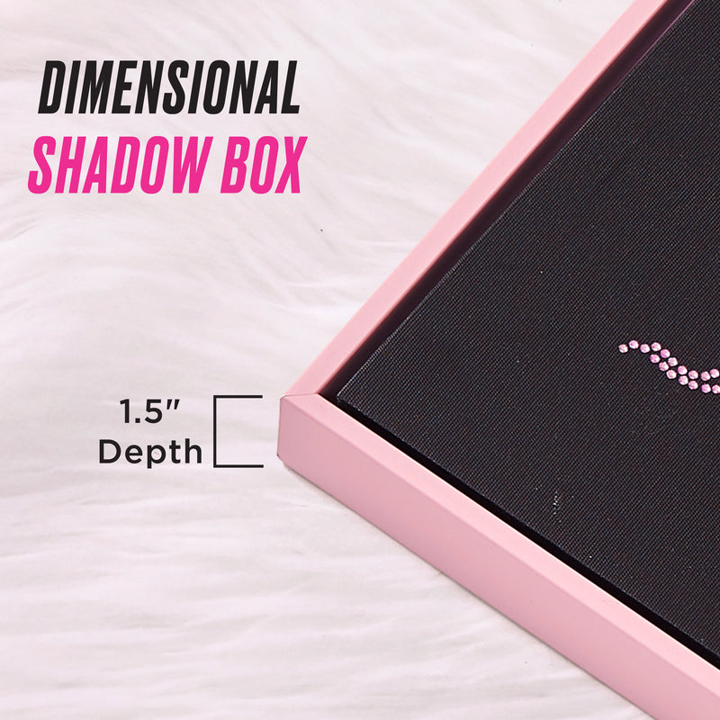 Close-up of a Shadow Box Wall Art, 16″ x 20″, featuring a pink frame with black art inside, placed on a white textured surface. This fashion-inspired piece adds Juicy Couture wall art flair to your home. Text reads: DIMENSIONAL SHADOW BOX and 1.5″ Depth, accompanied by a depth illustration.