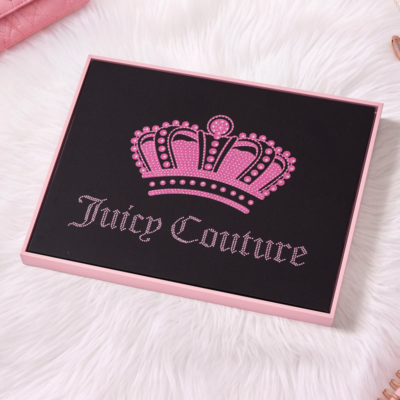 A 16″ x 20″ Shadow Box Wall Art featuring a black and pink Juicy Couture box adorned with a jeweled pink crown and the brand’s cursive name, displayed on a white fur surface—perfect as chic, fashion-inspired decor to elevate your space.
