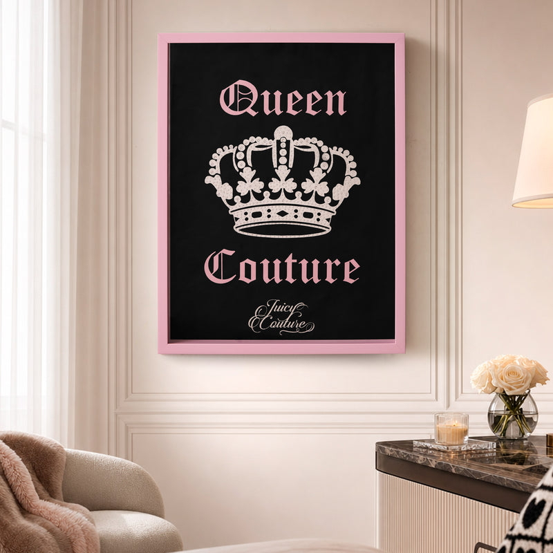 The Shadow Box Wall Art, 18″ x 24″, featuring a crown and the words “Queen Couture” in pink with “Juicy Couture” beneath, hangs above a side table adorned with roses and a lamp in an elegant room. This fashion-inspired decor piece adds a touch of glamour to the sophisticated setting.