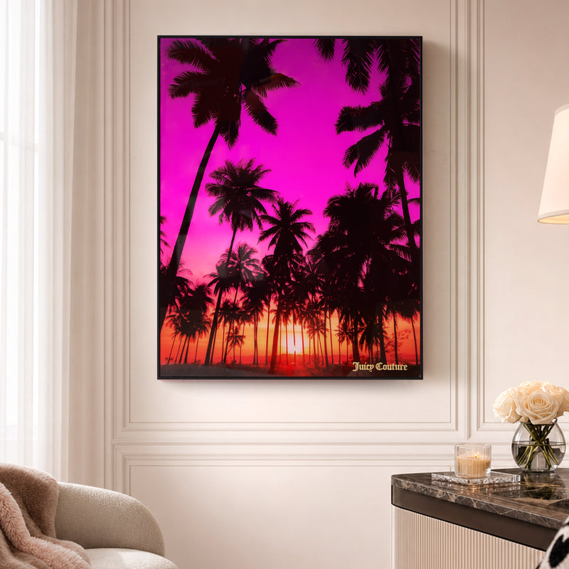 A Shadow Box Wall Art, 18″ x 24″, featuring a serene scene of palm trees at sunset with a pink and orange sky, hangs on a beige wall above a marble table adorned with a flower arrangement and candle, bringing chic elegance to the space.