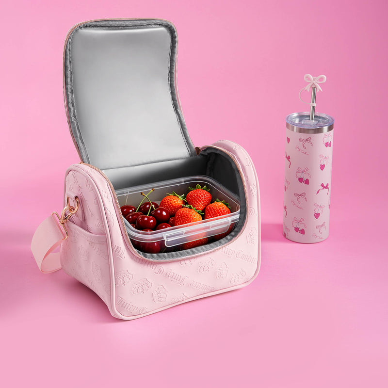 A pink Lunch Purse Cooler Bag, decorated with cherries and strawberries, sits alongside a matching pink tumbler with a straw on a vibrant pink background. The clear container inside the Juicy Couture Lunch Purse Cooler Bag keeps your snacks fresh while adding a playful touch of style.