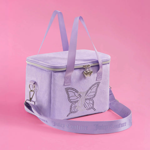 A stylish Chill Couture Cooler Bag in lavender by Juicy Couture, featuring a rhinestone butterfly design, heart-shaped zipper pull, and matching shoulder and hand straps, sits elegantly on a pink background.