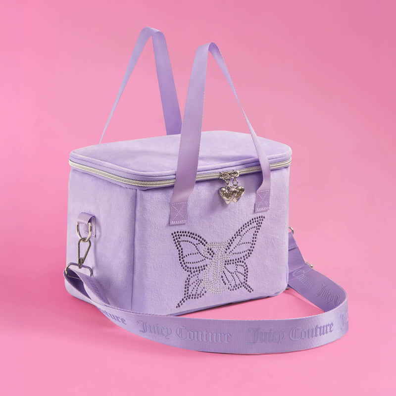 A stylish Chill Couture Cooler Bag in lavender by Juicy Couture, featuring a rhinestone butterfly design, heart-shaped zipper pull, and matching shoulder and hand straps, sits elegantly on a pink background.