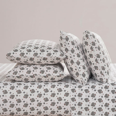 A neatly made bed features the Microfiber Sheet Set With Extra Pillowcases, showcasing white bedding adorned with a repeating pattern of small black and gray hedgehogs and tiny red hearts on all pillows.