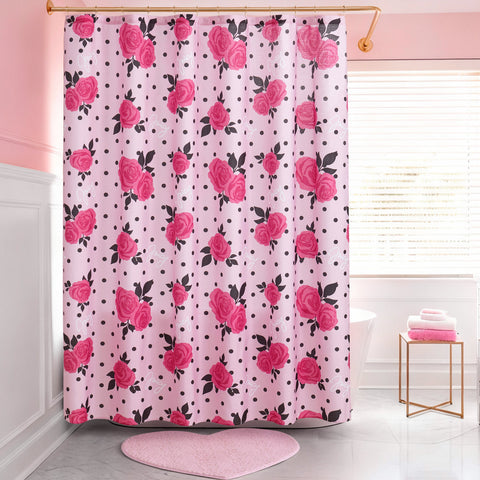 A pink bathroom with a Shower Curtain and Hooks Set featuring red roses and black polka dots, a pink heart-shaped rug, white tub, folded towels on a stool, and a window with white blinds.