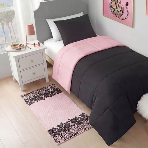 A modern bedroom featuring a neatly made bed with a pink and black comforter, black pillow, white nightstand with makeup and lamp, wall art of a leopard, and a Finely Washable Rug, 2' x 4', in a pink and black floral pattern.