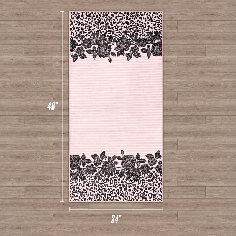 The Finely Washable Rug, 2' x 4', is rectangular and ultra-soft with a pale pink background, black floral rose borders, bold black leopard print at the top and bottom, and is shown on a wooden floor.