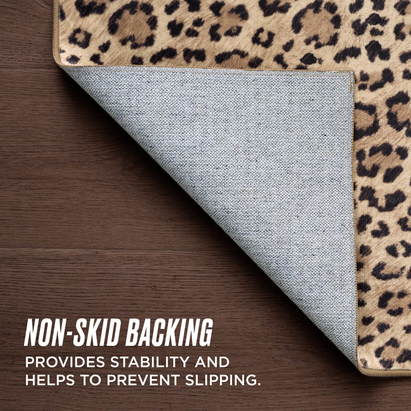 The Finely Washable Rug, 2' x 4', is shown in leopard print with a corner lifted to display its textured, gray non-skid backing on a wooden floor. Text: NON-SKID BACKING provides stability and helps prevent slipping.