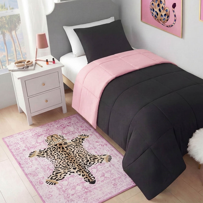 A neatly made bed with a black and pink comforter sits beside a white nightstand with a lamp and nail polish. On the floor, the Finely Washable Rug, 3' x 5', shows off its pink leopard print beneath leopard artwork on the wall.