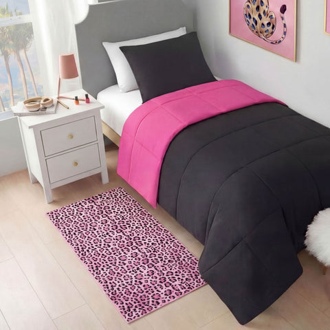 A neatly made bed with black and bright pink bedding sits beside a white nightstand topped with a lamp and makeup items. A Finely Washable Rug, 2' x 4', in pink leopard print covers the light wood floor. Leopard wall art hangs above the bed.