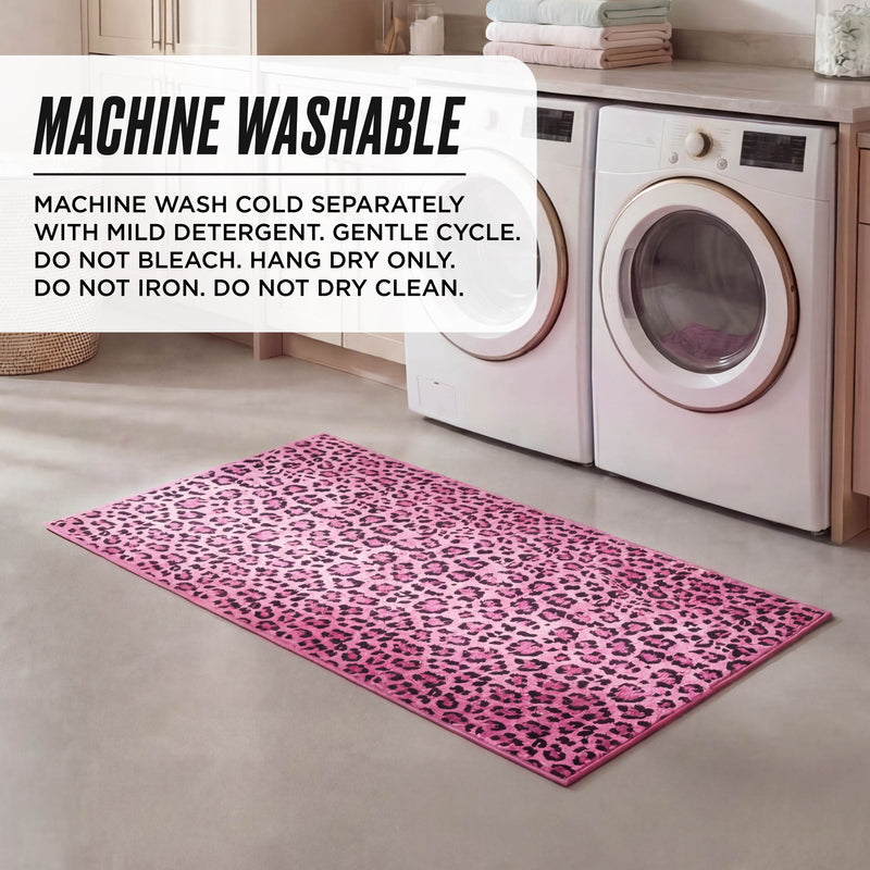 A Finely Washable Rug, 2' x 4', with a pink leopard print, is placed in front of a white washer and dryer in a laundry room; text in the image lists machine-washing instructions for this ultra-soft, machine-washable rug.
