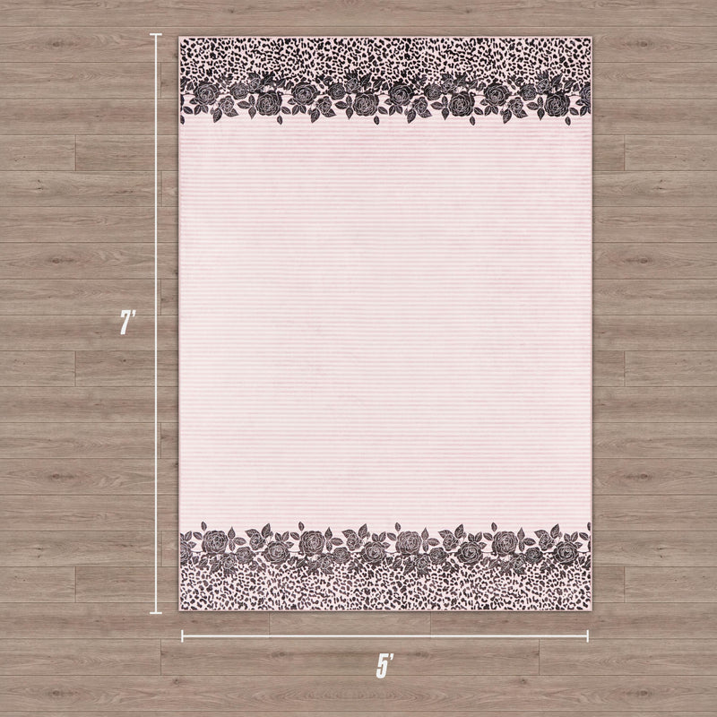 The Finely Washable Rug, 5' x 7', features a rectangular ultra-soft pink design with floral and leopard print borders on two sides, perfect for adding a chic touch to a room's wooden floor.