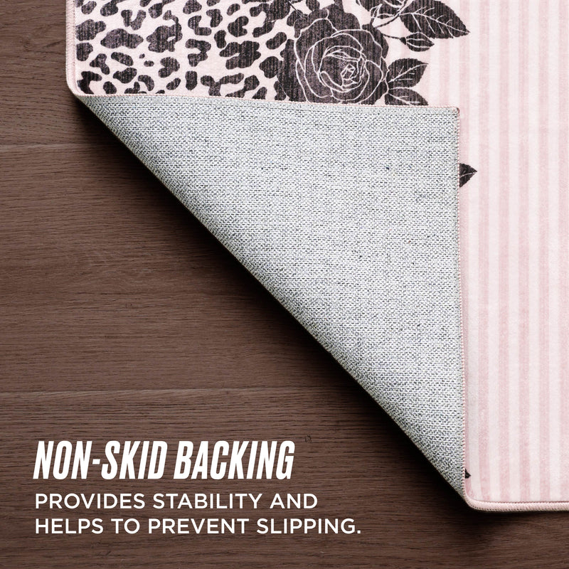 A Finely Washable Rug, 5' x 7', with floral and leopard print corner lifted to reveal its textured, non-skid backing on a wooden floor. Text: NON-SKID BACKING provides stability and helps prevent slipping.