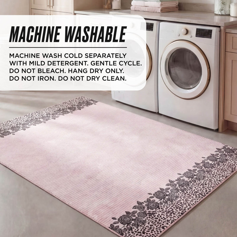 The Finely Washable Rug, 5' x 7', in light pink with floral and leopard print borders, is shown in a laundry room by the washer and dryer. Text overlay gives machine washing instructions for this ultra-soft, machine-washable rug.