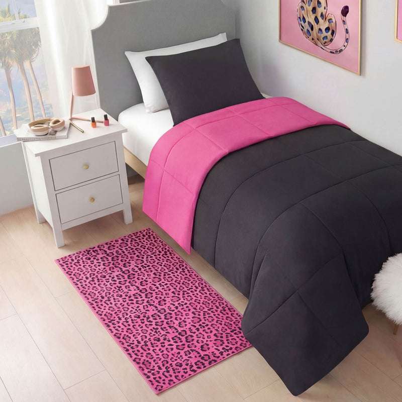 A neatly made twin bed with a dark gray and hot pink comforter sits beside a white nightstand. On the floor is a Finely Washable Rug, 2' x 4', featuring pink leopard print to match the leopard artwork above the bed.
